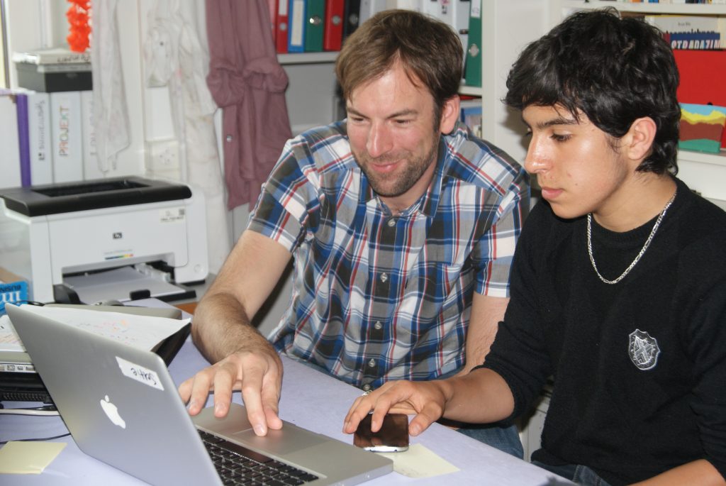 Kursleiter hilft einem Schüler beim Filmschnitt am Laptop
