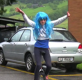 Szene aus einem Musikvideo: Darstellerin mit blauer Perücke auf dem Einrad