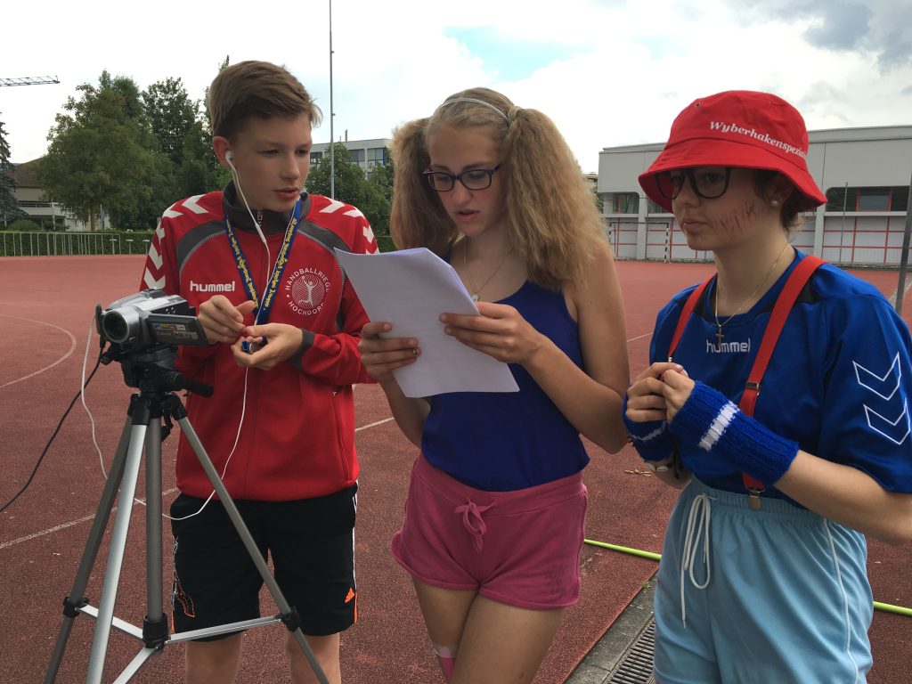 Drei Jugendliche besprechen am Set das Drehbuch neben der Kamera auf dem Stativ