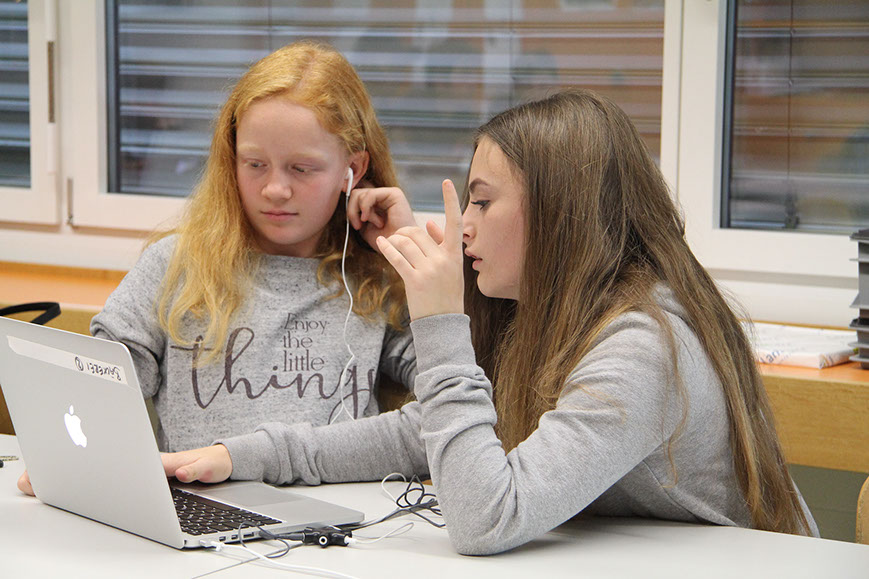 Zwei Schülerinnen schneiden mit Kopfhörern ihren Film am Laptop