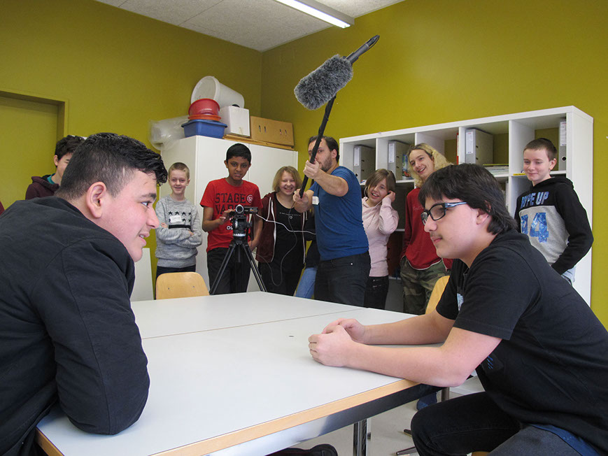 Filmdreh im Klassenzimmer: Zwei Schüler spielen eine Szene am Tisch, die Klasse schaut zu