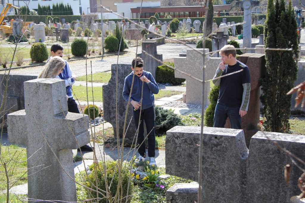 Jugendliche suchen auf einem Friedhof nach Drehorten zwischen den Grabsteinen