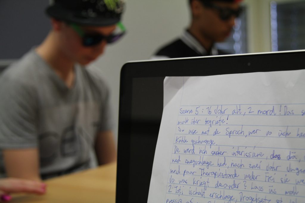 Handgeschriebenes Drehbuch im Vordergrund, Darsteller mit Sonnenbrille im Hintergrund