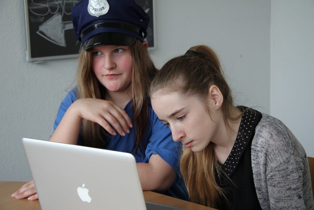 Zwei Schülerinnen, eine davon mit Polizeimütze, sichten ihr Filmmaterial am Laptop