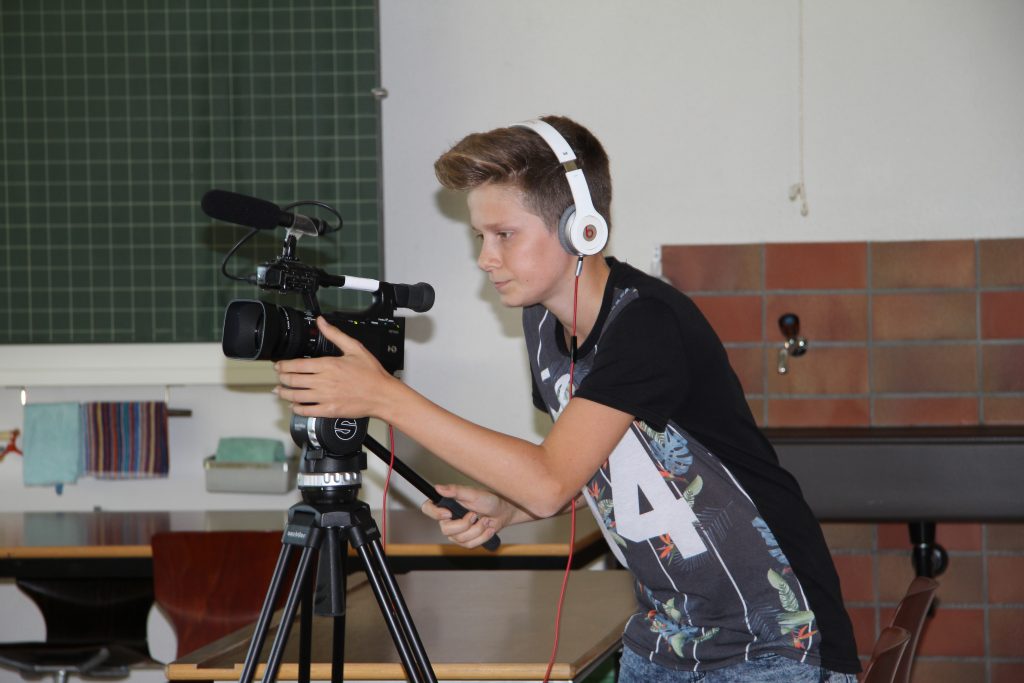Schüler mit Kopfhörern bedient eine Videokamera mit Mikrofon im Schulzimmer