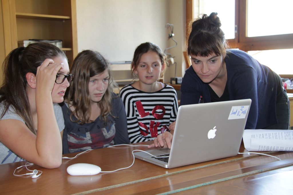Kursleiterin unterstützt drei Schülerinnen beim Filmschnitt am Laptop