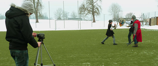 Musikvideo-Dreh im Schnee: Darsteller in Ritterkostümen kämpfen, ein Schüler filmt